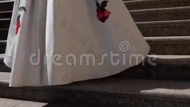 一个女人穿着一条镶着红花的白色裙子走<strong>上台</strong>阶。 用石头做的台阶和栏杆。